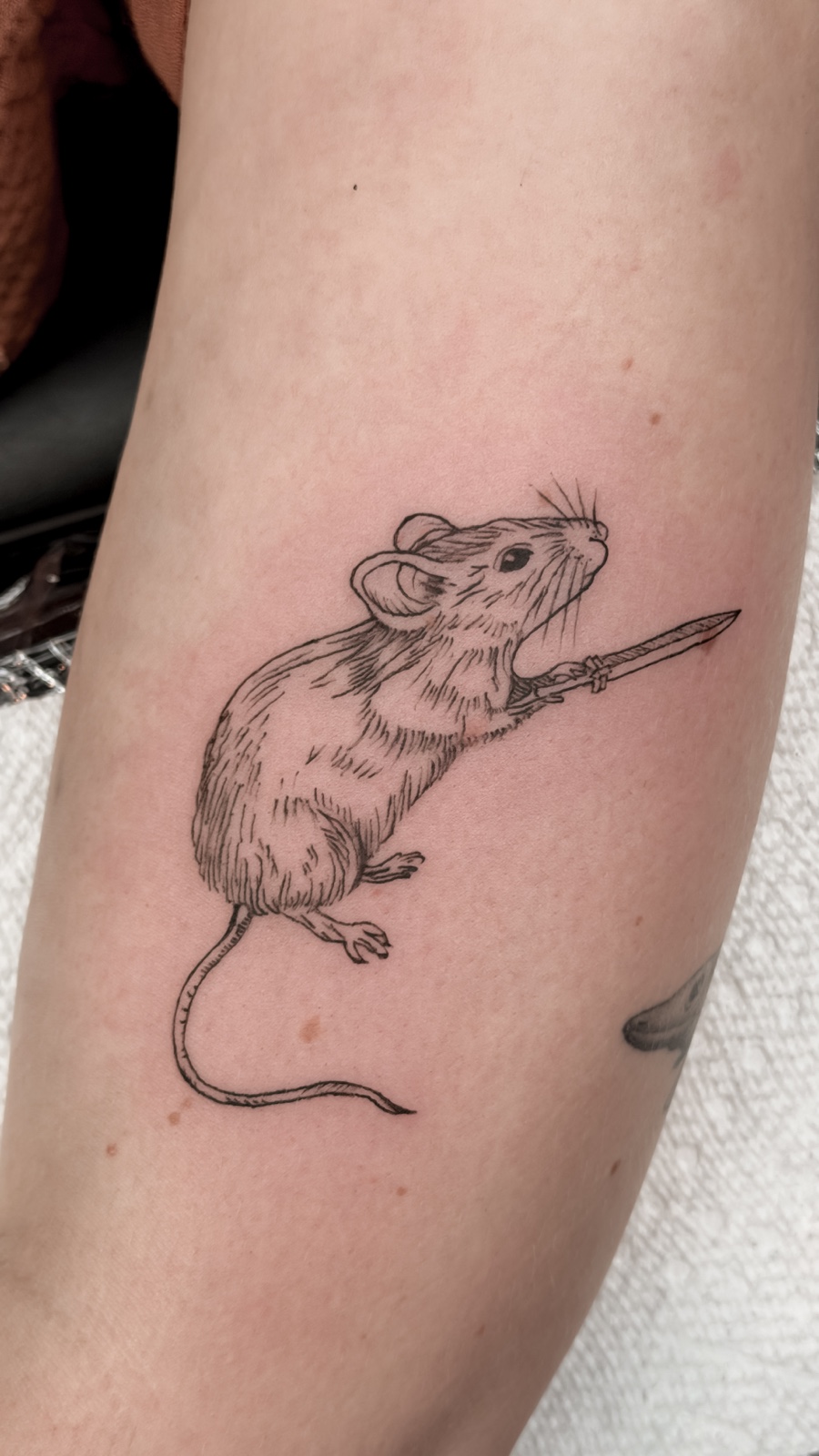 Fine-line mouse tattoo holding a small sword